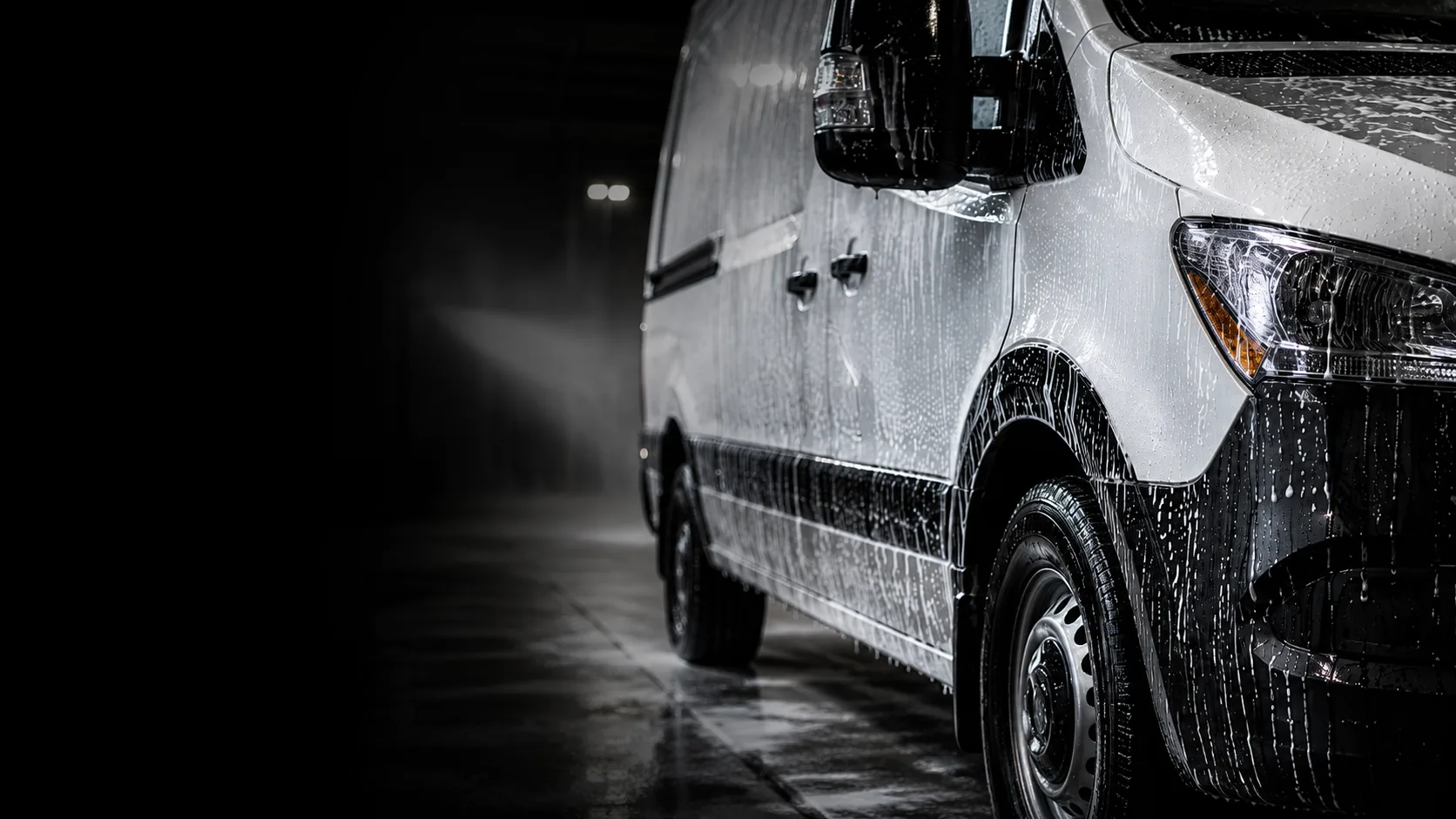 Commercial fleet van being washed in a professional wash bay with dramatic lighting
