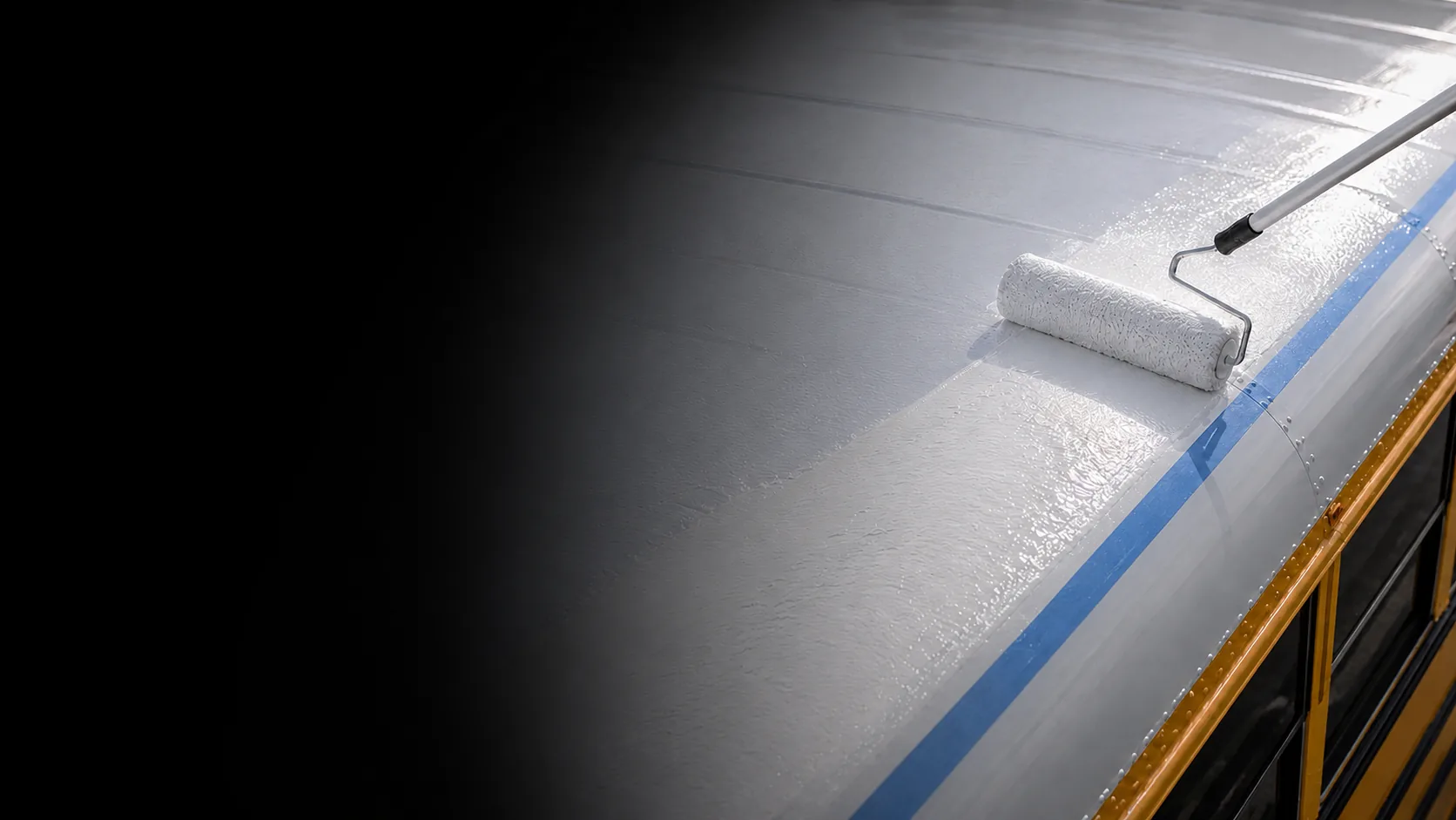 Roller applying white reflective roof coating to a school bus roof